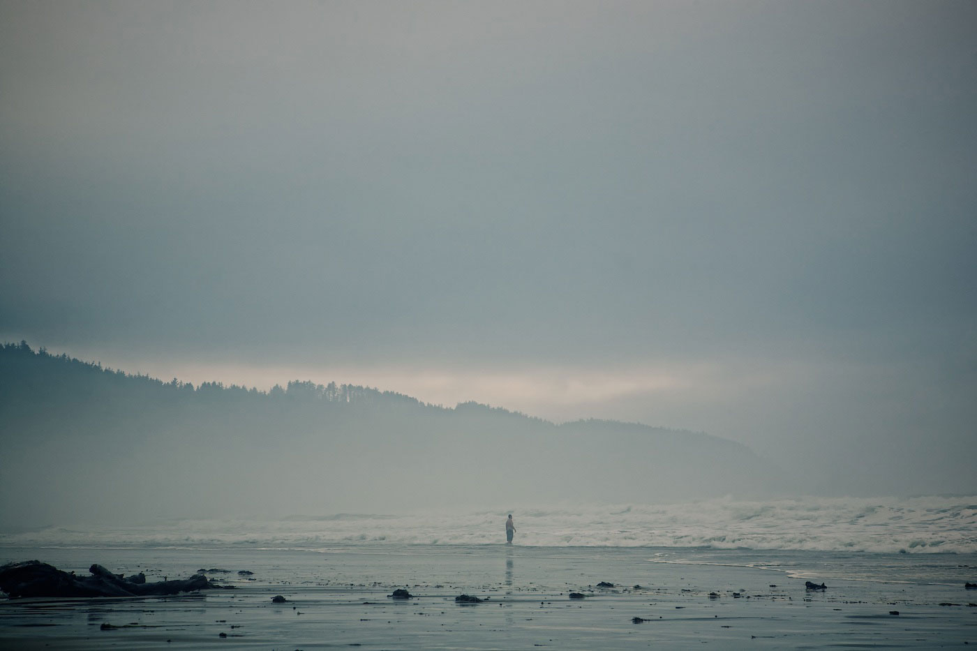 A surfer stand on the beach in foggy weather.