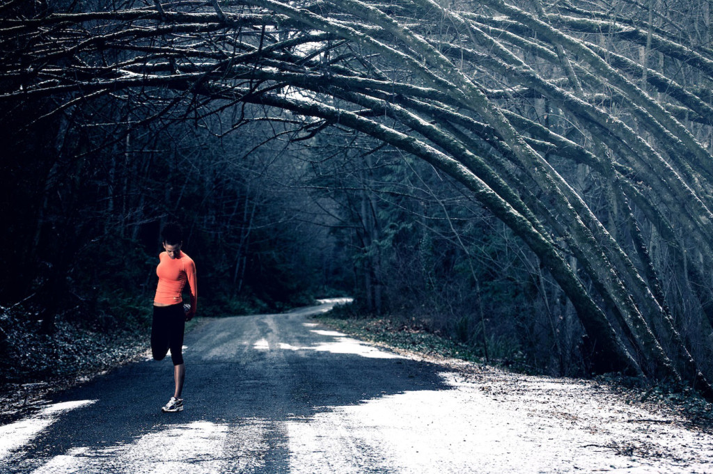 A runner stretches under an arch made of trees.