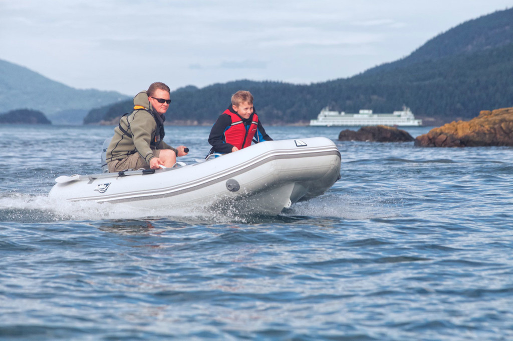 A man and his son are in a small rubber boat, zooming across the water.